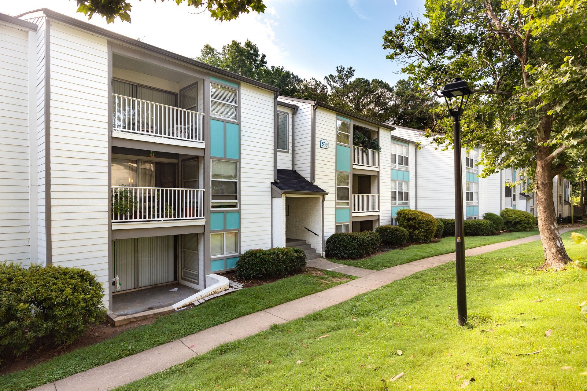 Apartment building with balconies and a grassy walkway lined by trees