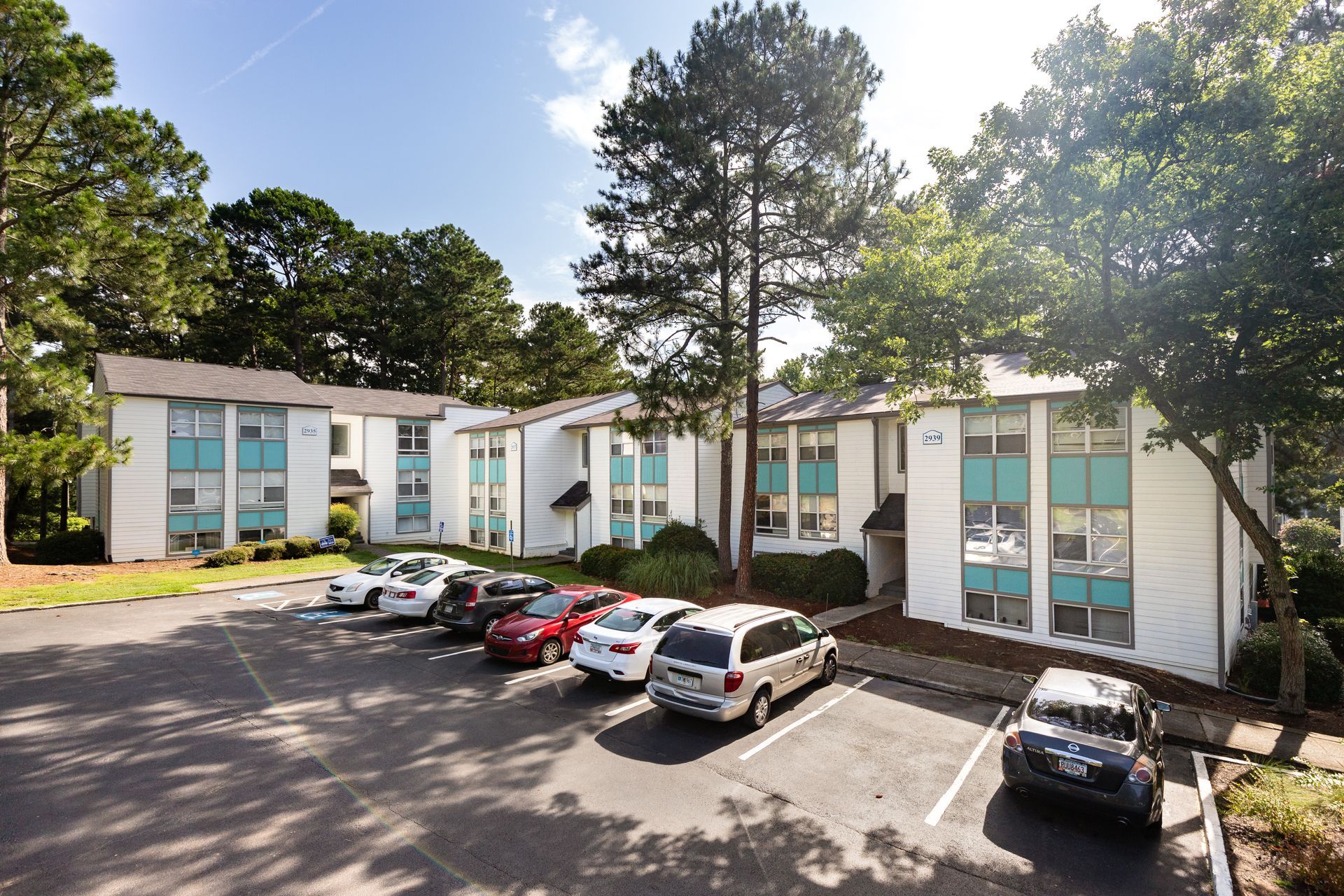 Apartment complex with parked cars, tall trees, and sunny blue-sky courtyard