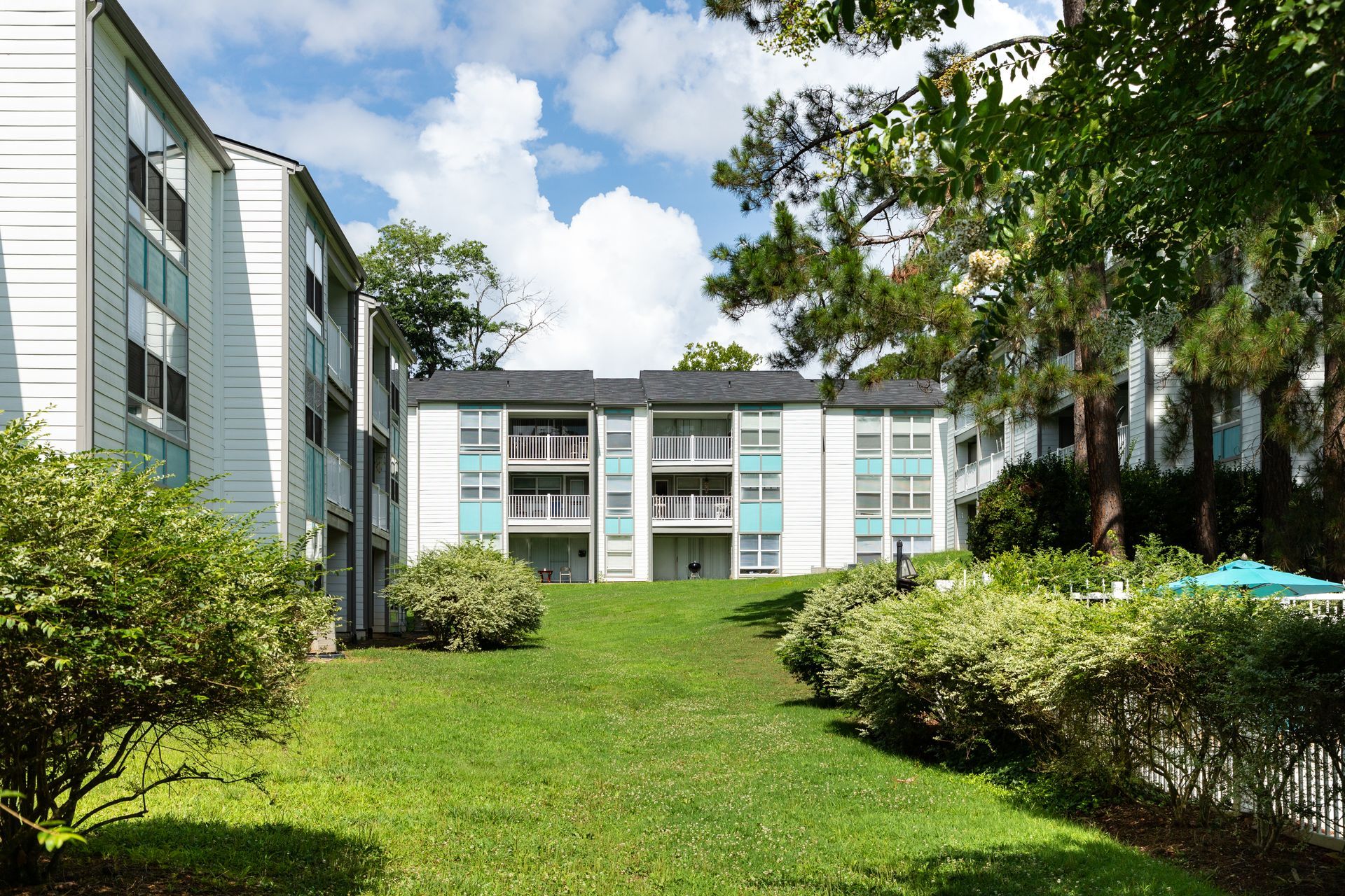 Apartment complex courtyard with green lawn, shrubs, and blue sky between white buildings