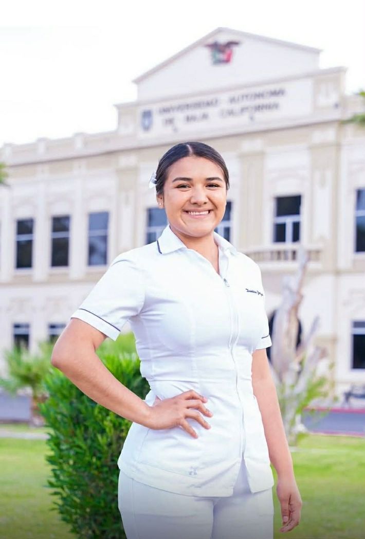 Smiling person in a white uniform standing outside a campus building