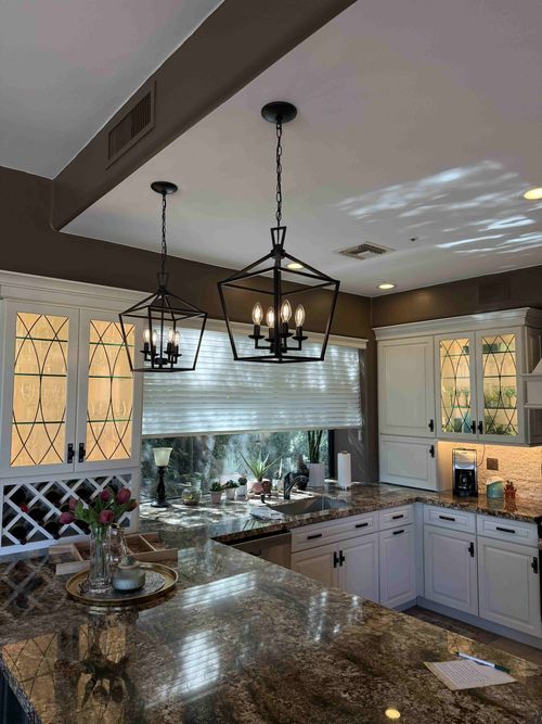 Bright kitchen with white cabinets, granite island, hanging lanterns, and a window over the sink