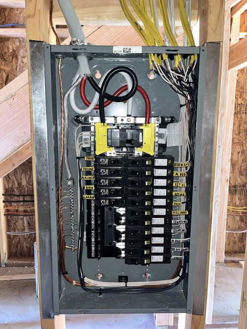 Open electrical breaker panel with exposed wiring and circuit breakers in a wall frame