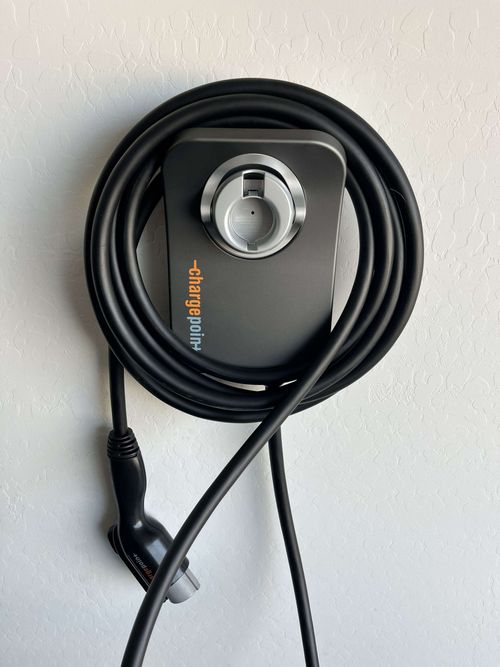 Coiled black charging cable with a gray connector and dial-like plug on a light surface
