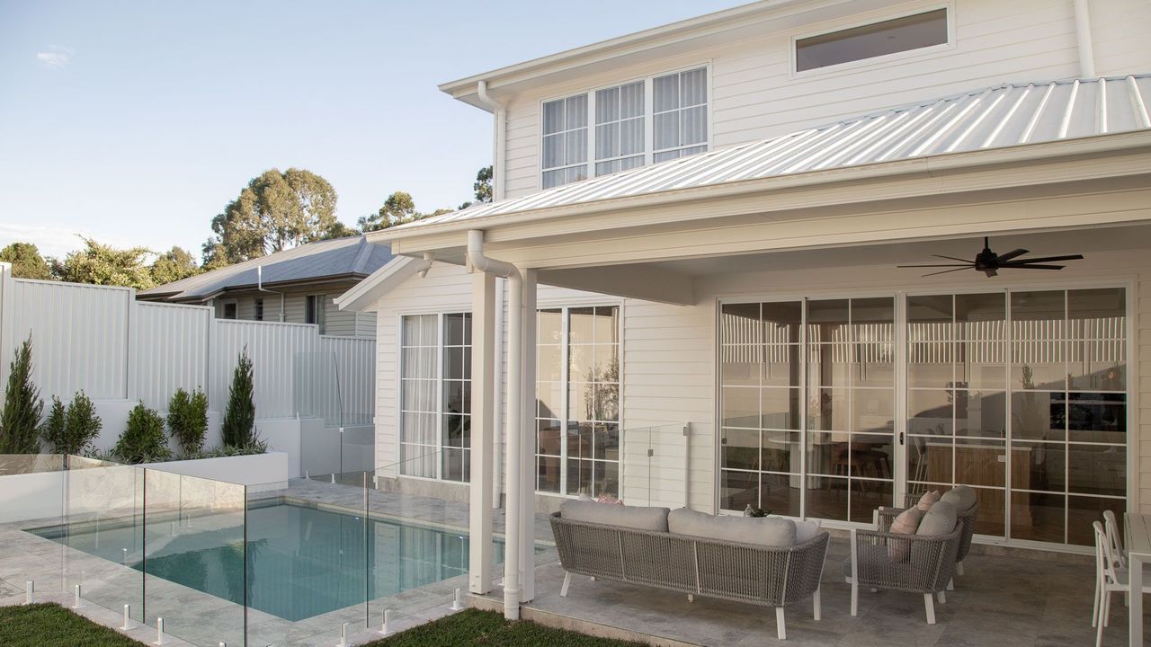 Backyard patio with pool, covered seating area, and two-story white house with sliding glass doors