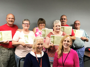 Group of people posing indoors with certificates, smiling at the camera.