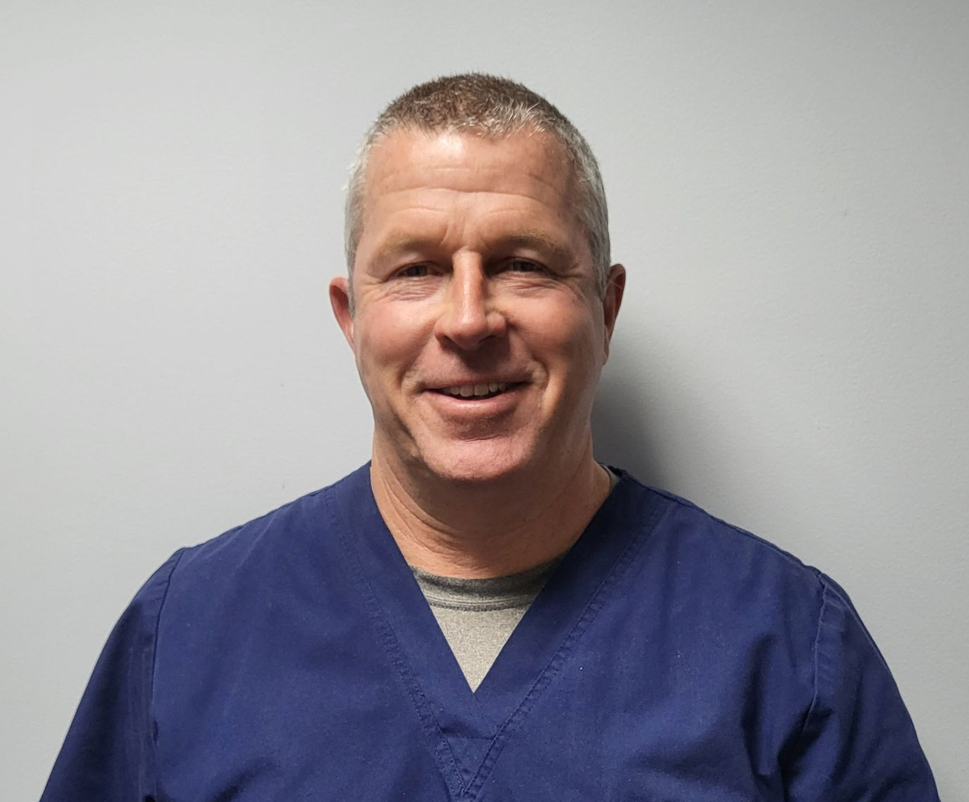 Picture of Dr. John Duffy.  Wearing a blue scrub top and grey t-shirt underneath. 