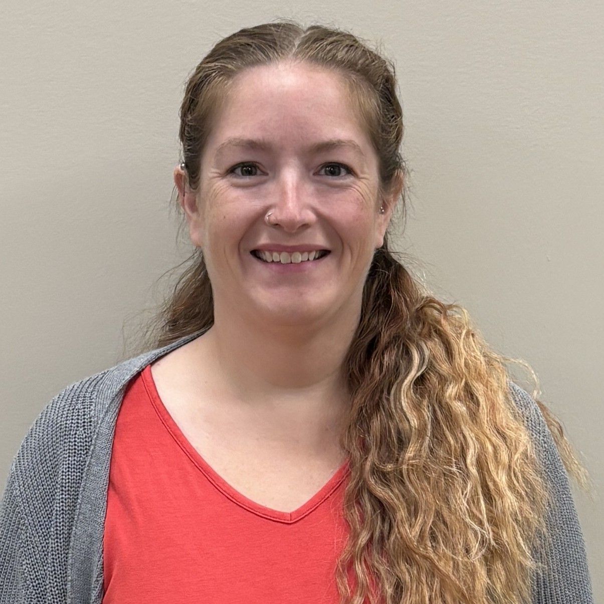 Head-and-shoulders profile photo of Emily Frank, Family Nurse Practitioner wearing a red top and a gray cardigan, photographed against a plain light-colored background.