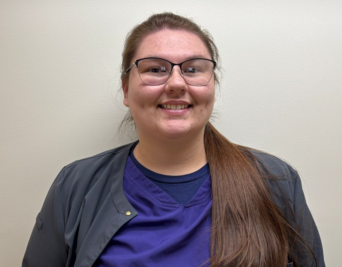 Professional profile photo of Francesca Wilson, Medical Assistant wearing glasses, a purple scrub top, and a dark jacket, photographed against a plain light-colored background.