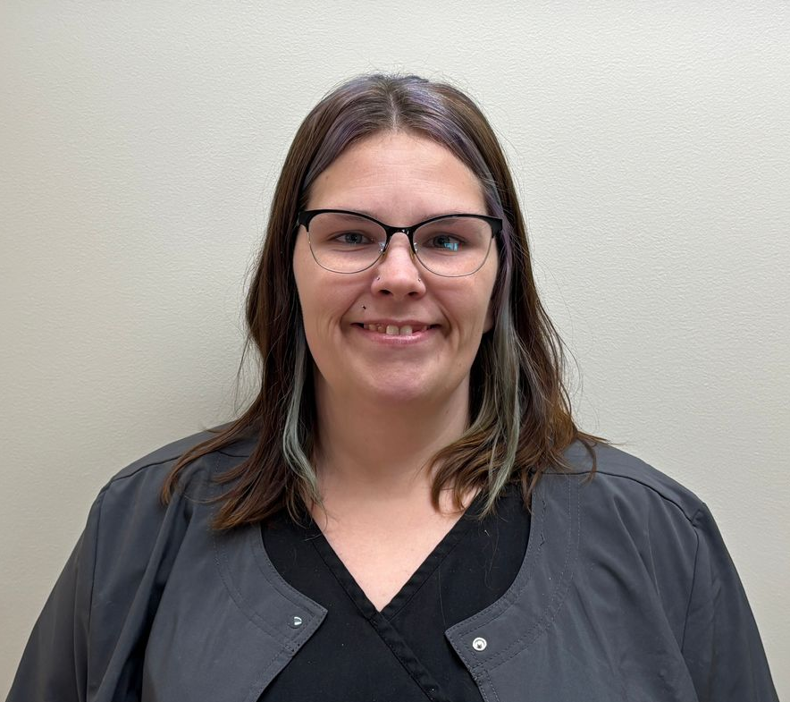 Head-and-shoulders profile photo of Leah Edwards, Medical Assistant wearing glasses, a dark top, and a gray jacket, photographed against a plain light-colored background.
