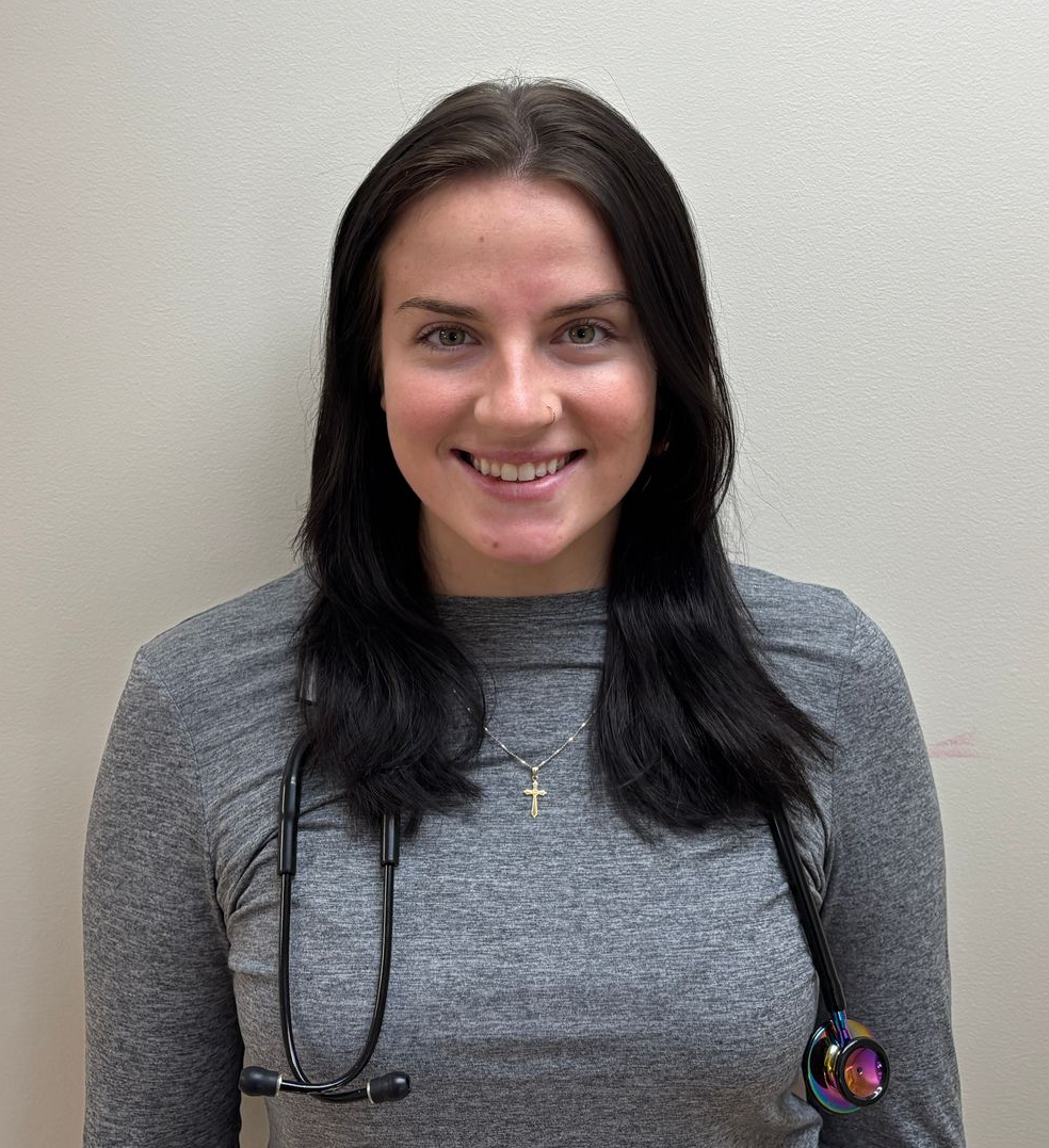 Head-and-shoulders profile photo of Riley Storrin, Medical Assistant wearing a long-sleeved gray top and a stethoscope, photographed against a plain light-colored background.
