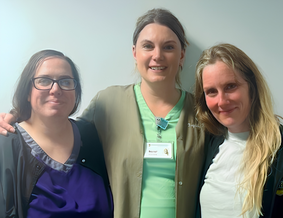 Three women standing together, smiling, in a bright indoor setting.