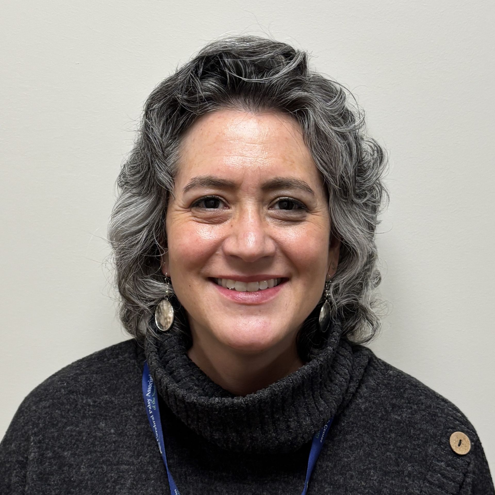 Profile photo of Sandina Vansleet, Dental Practice Manager wearing a dark textured sweater, earrings, and a lanyard, photographed against a plain light-colored background.