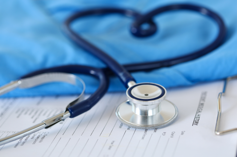 Close up photo of a stethoscope resting on medical paperwork, with blue gloves and clinical documents visible in the background.