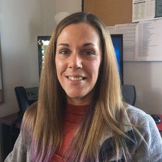 Head-and-shoulders profile photo of Melissa Bouchey, Care and Access Coordinator, Substance Use Services wearing a long-sleeved rust-colored top and a light gray cardigan, photographed indoors in an office setting with computer monitors and papers visible in the background.