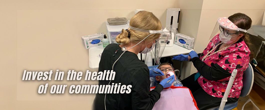 Photo of three people in a dental treatment room, with one person seated in a dental chair while two others stand nearby wearing protective equipment, overlaid with the text “Invest in the health of our communities.”