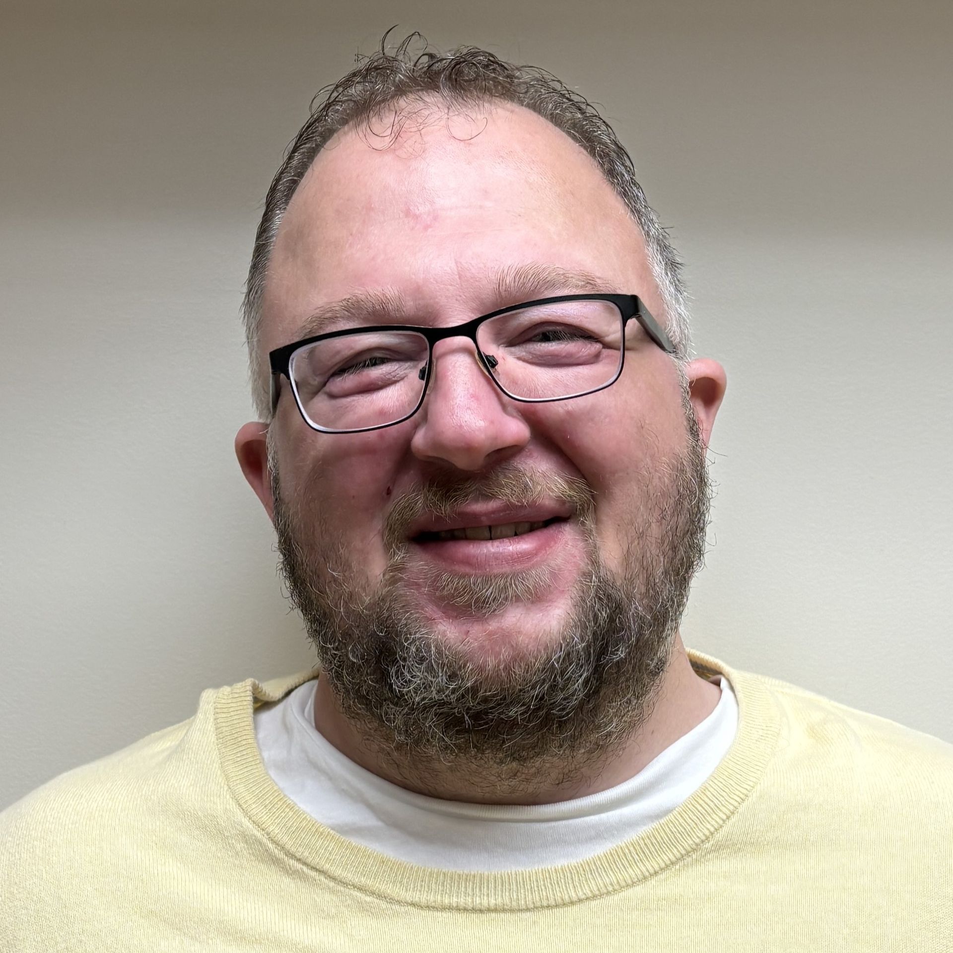 Head-and-shoulders profile photo of Jason Matice, RN, Transitional Care Management wearing glasses and a light yellow sweater over a white shirt, photographed against a plain light-colored background.