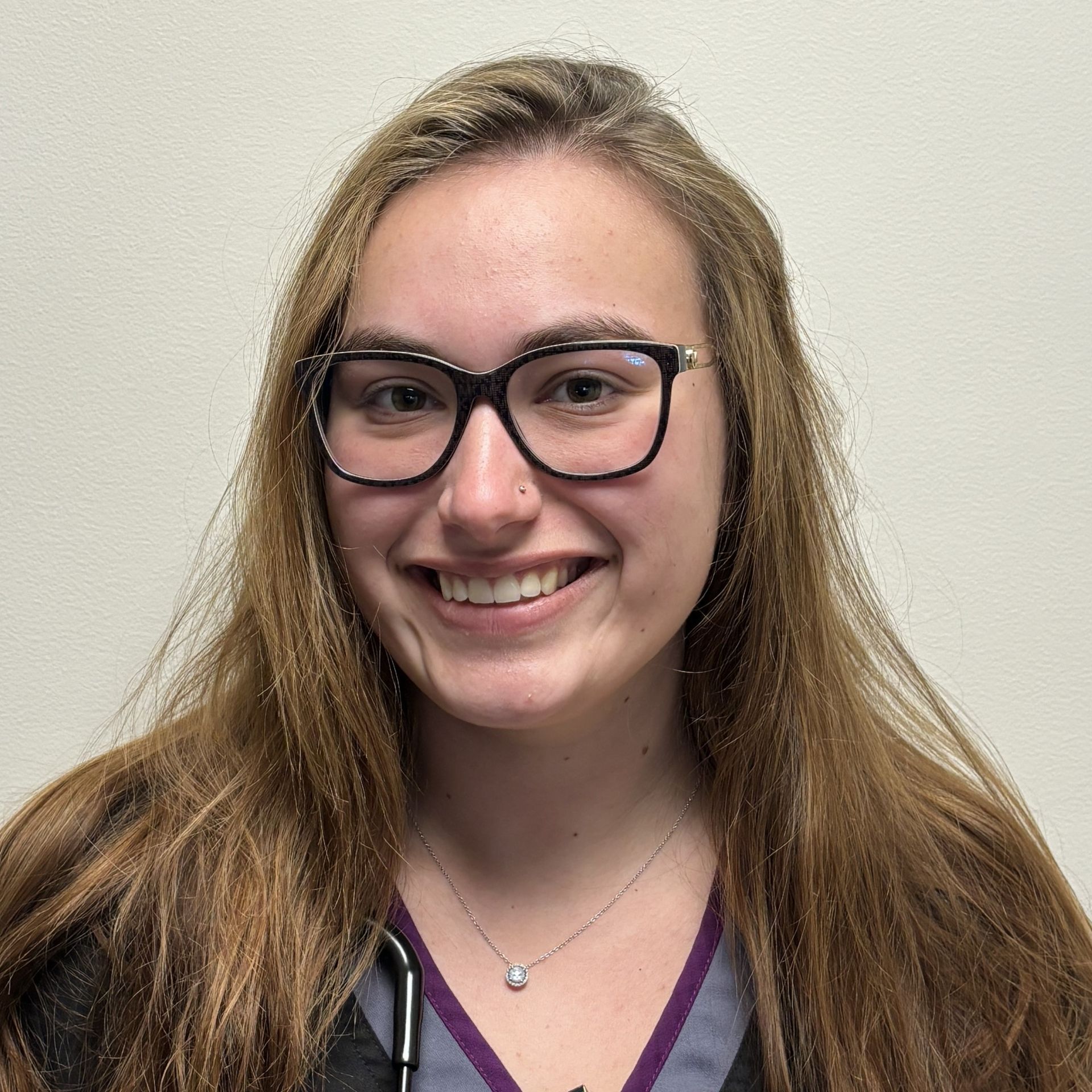 Professional profile photo of Brandi Walrath, Medical Assistant wearing glasses, a dark scrub top with purple trim, and a stethoscope, photographed against a plain light-colored background.