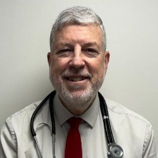 Profile photo of Dr. Donald Schuessler, MD wearing a light dress shirt, a red tie, and a stethoscope, photographed against a plain light-colored background.  Member of the pediatric team at the Gouverneur Health Center.