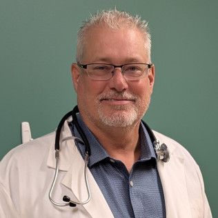 Head-and-shoulders profile photo of Dr. Richards, DO wearing glasses, a white medical coat with a stethoscope, and a blue collared shirt, photographed against a plain green background.