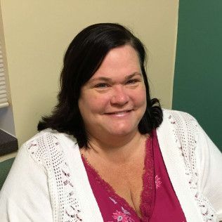 Head-and-shoulders profile photo of Marcia Raville, Licensed Clinical Social Worker wearing a pink top and a white open- knit cardigan, photographed indoors against a neutral-colored background.