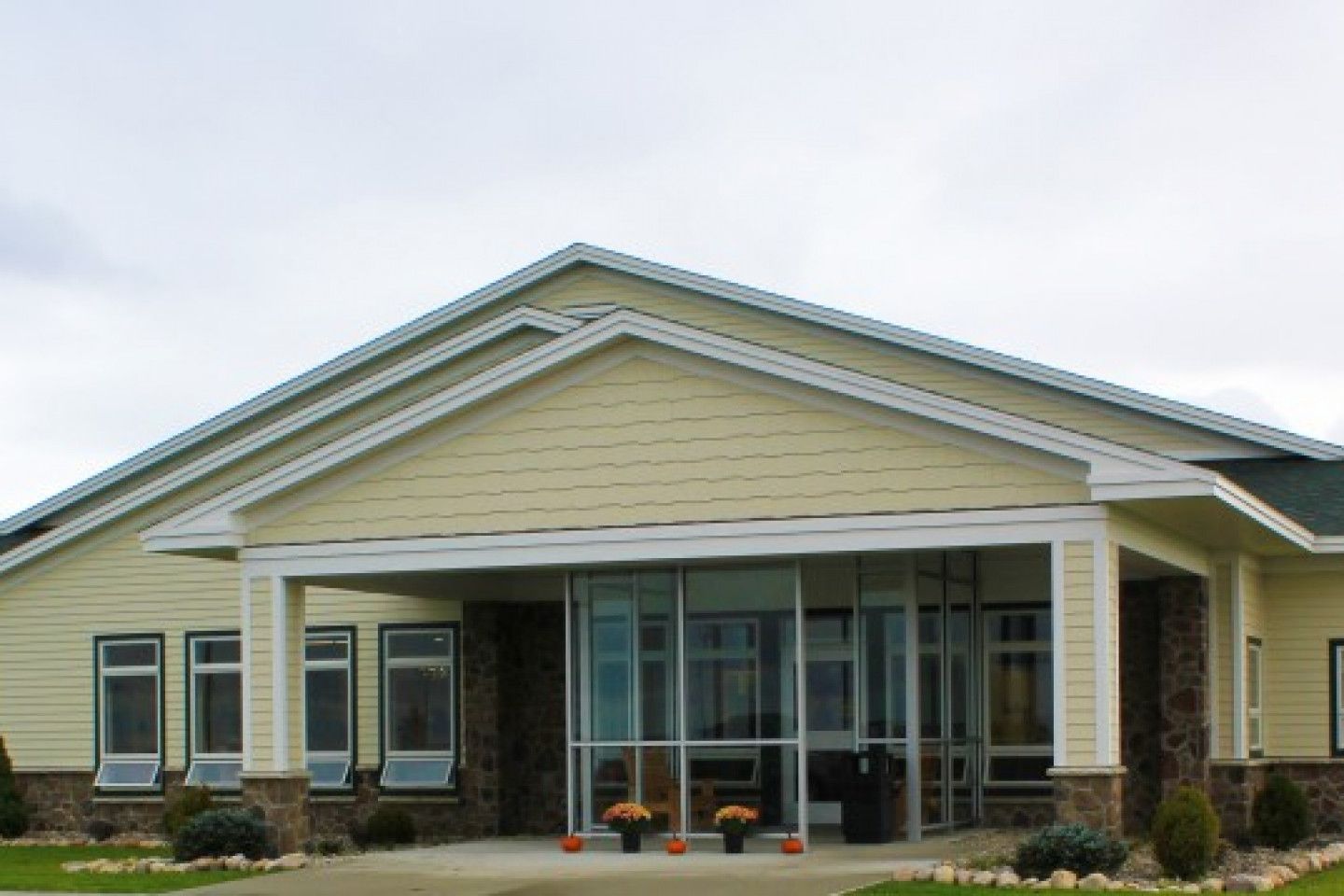 Exterior view of our single-story health center in Malone with a gabled roof and a covered entrance, featuring large glass doors, multiple windows, and landscaping along the front.