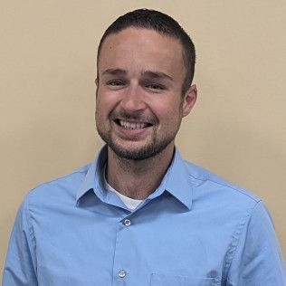 Head-and-shoulders profile photo of Derek Fenton, Family Nurse Practitioner wearing a light blue button‑down shirt, photographed against a plain beige background.