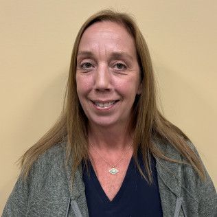 Head-and-shoulders profile photo of Christine Schneider, Medical Assistant wearing a dark top and a green cardigan, photographed against a plain beige background.