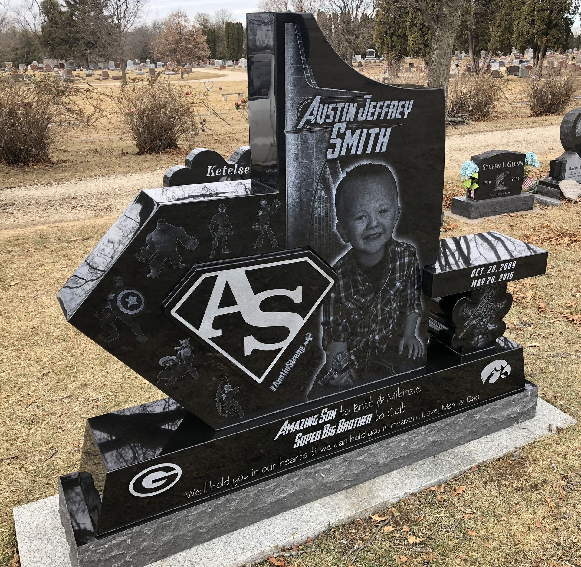 A black granite headstone with a portrait, a superhero-style