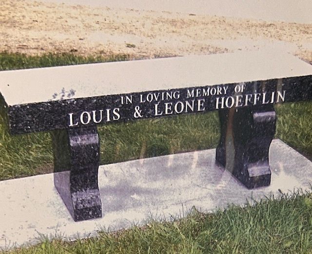 A granite memorial bench on a concrete base, inscribed