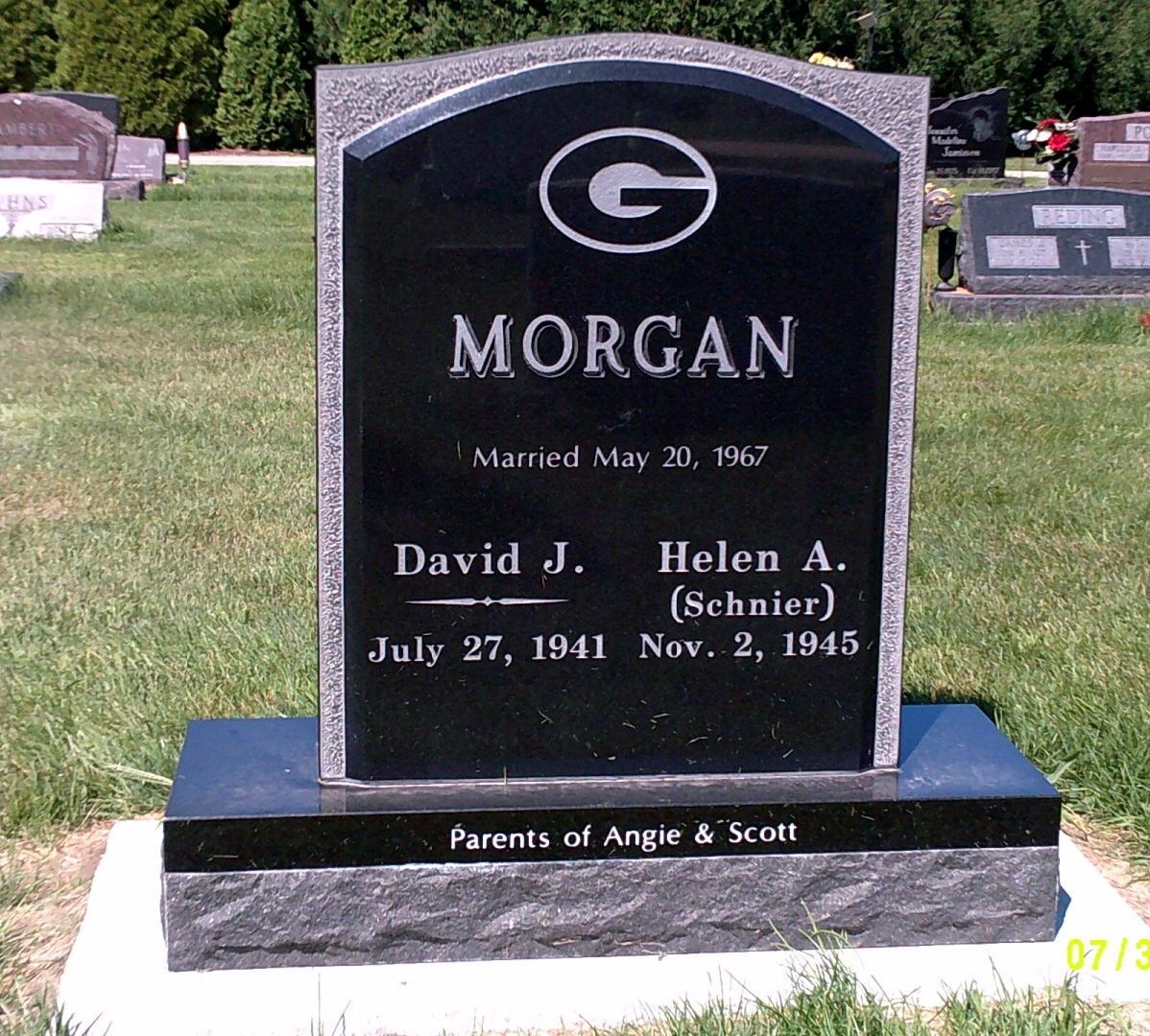 A black granite headstone for the Morgan family in a cemetery, featuring a Green Bay Packers logo, dates, and names.