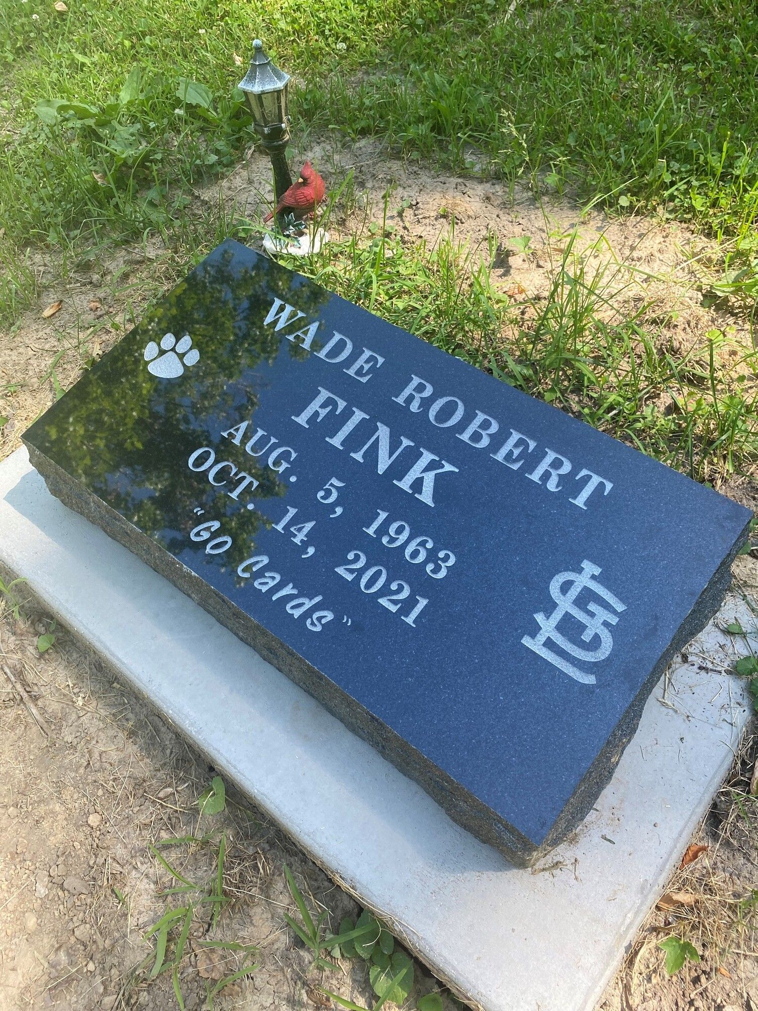 A black granite grave marker for Wade Robert Fink (1963-2021) with a small street lamp ornament and a cardinal figurine.