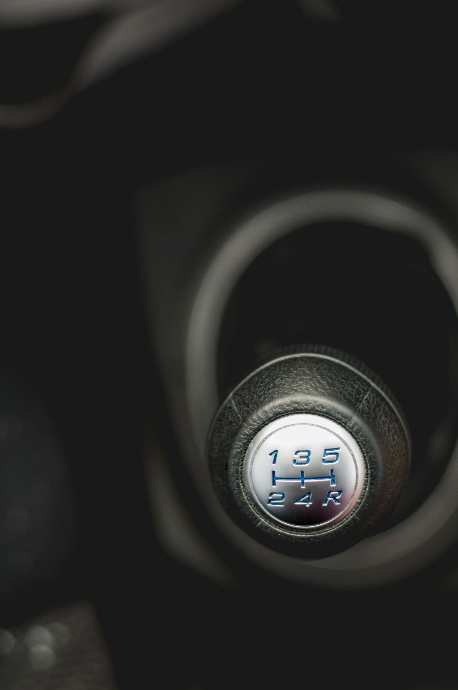 Close-up of a car's gear shift knob, showing gear positions 1-5 and reverse, against a dark background.