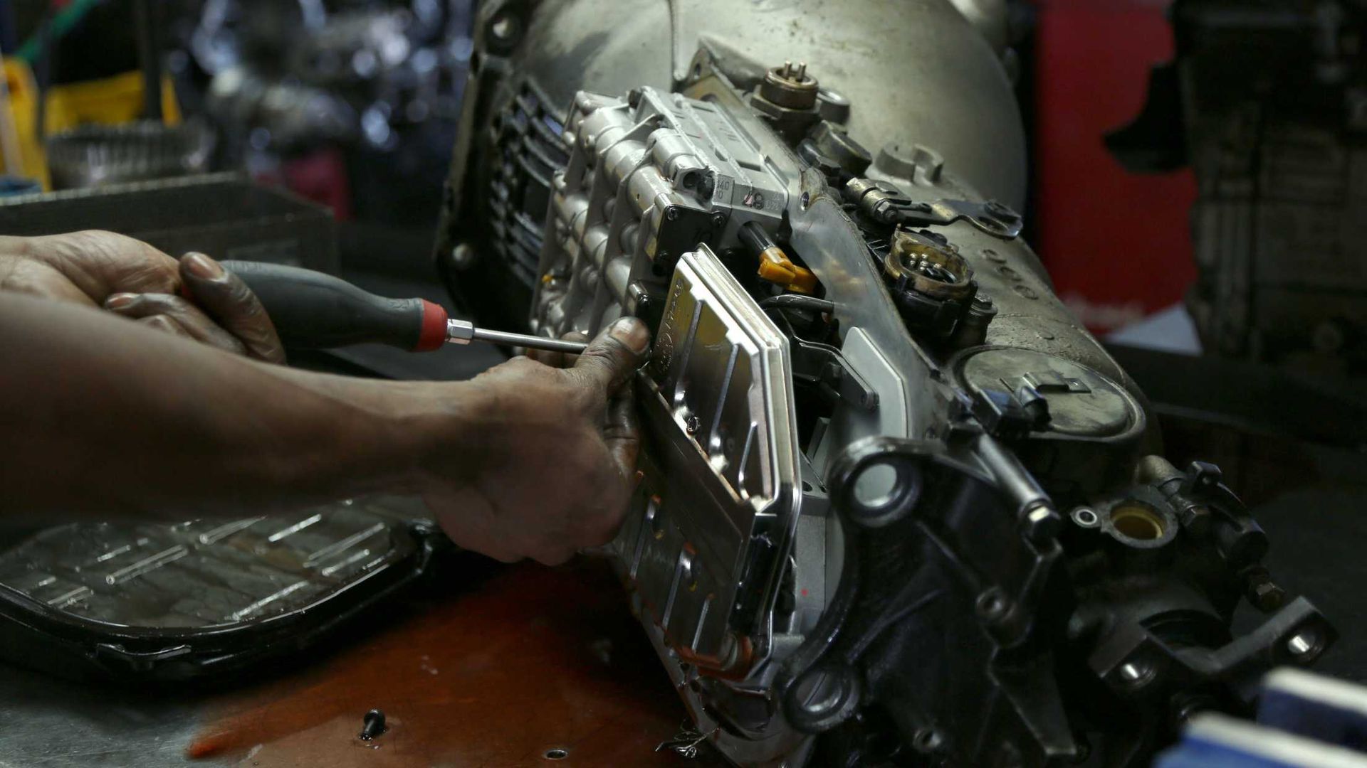 Mechanic disassembling a car transmission with a screwdriver in a workshop.