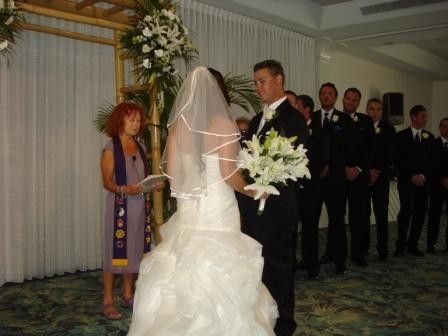 Bride and groom exchanging vows at a wedding altar, with attendants standing nearby