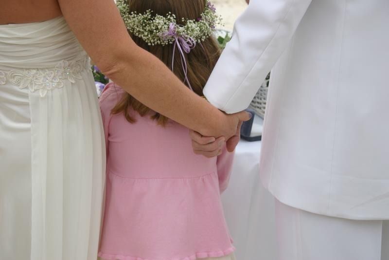 Three people holding hands at a wedding, including a child in a pink dress