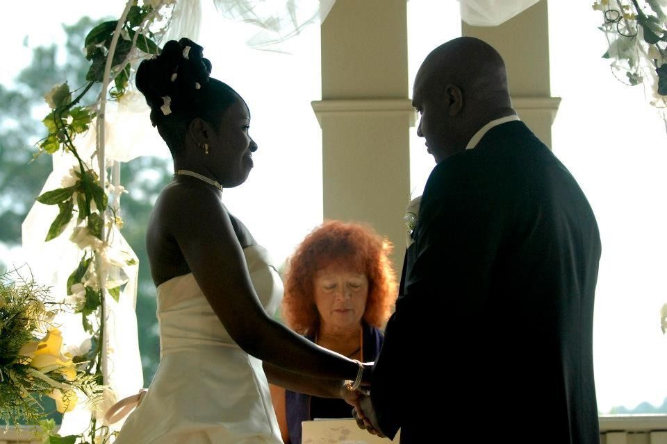 Couple holding hands during an outdoor wedding ceremony, officiant standing between them