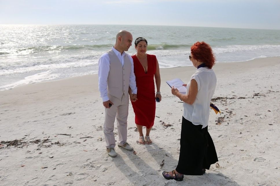 Three people talking on a bright beach, with the ocean and wet sand behind them.
