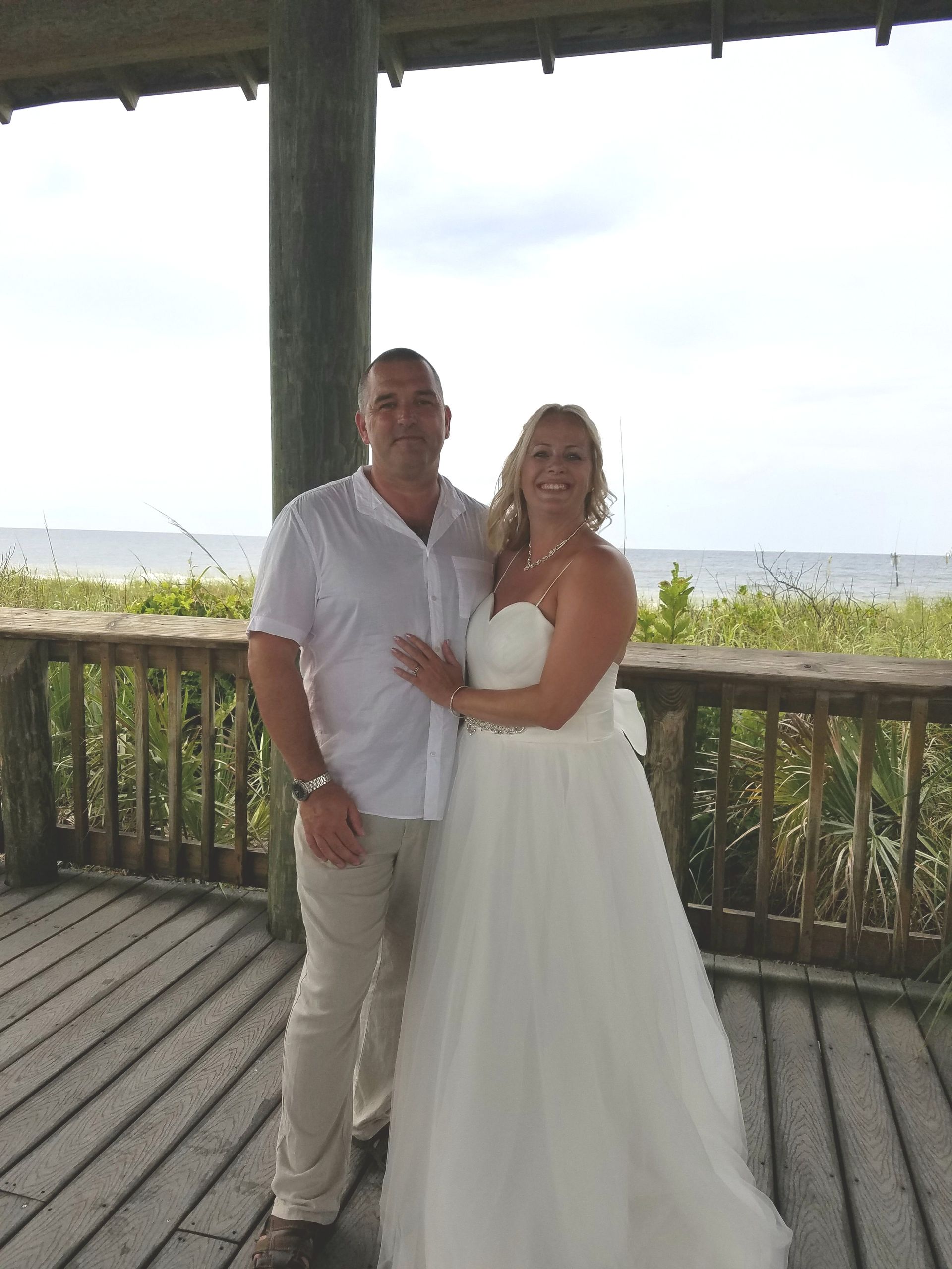 Couple posing on a gazebo with ocean view, the woman in a white dress and the man in a white shirt and tan pants