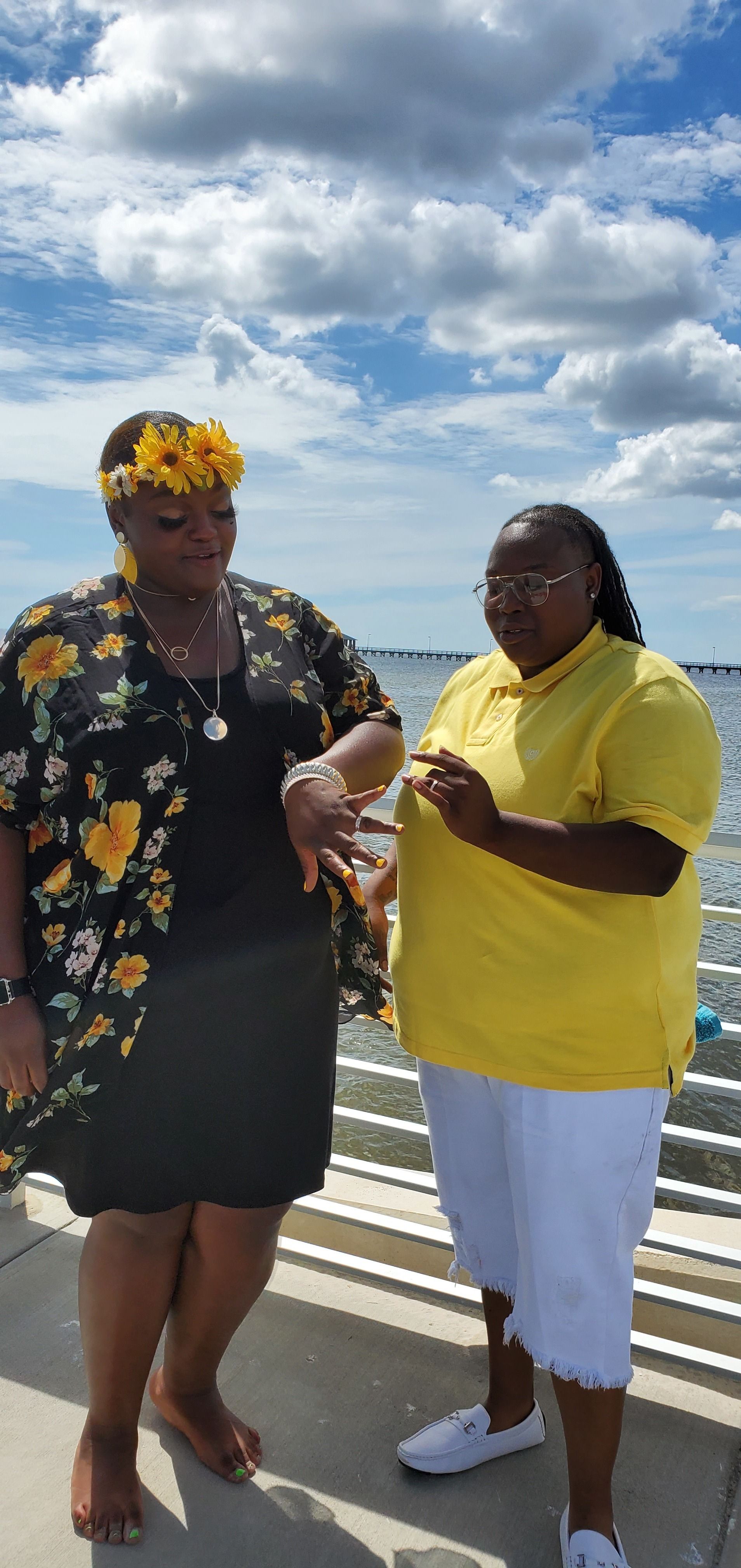 Two people on a beach boardwalk, one holding flowers, under a cloudy sky