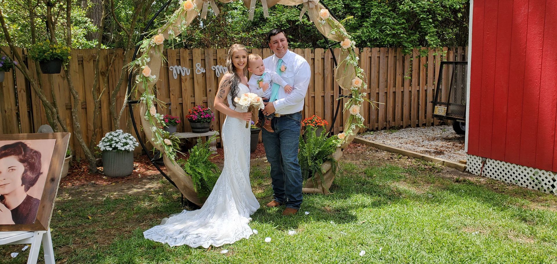 Bride and groom holding a bouquet under a heart-shaped arch in a backyard garden