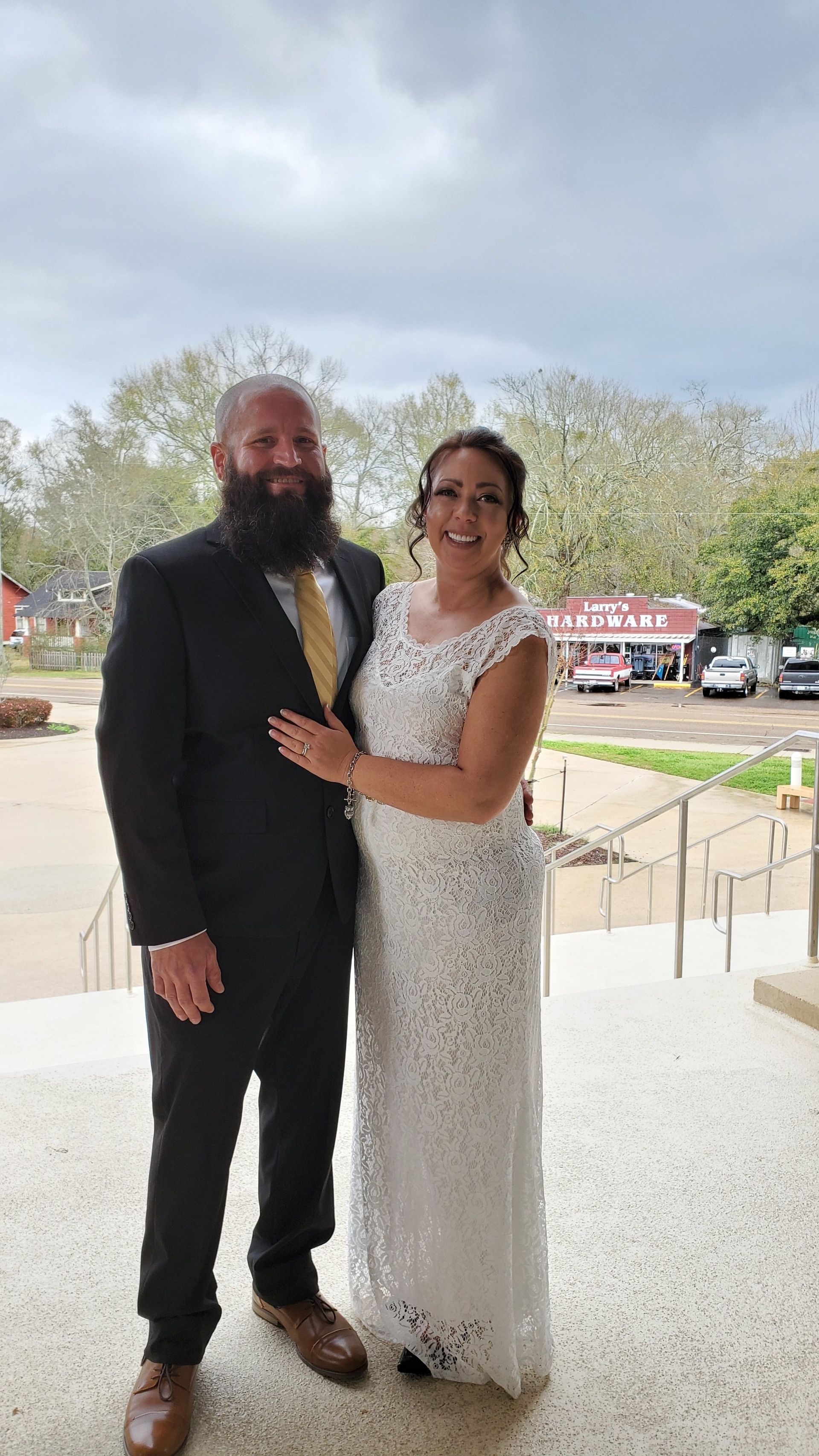 Couple dressed formally outdoors, standing together and smiling near a building entrance