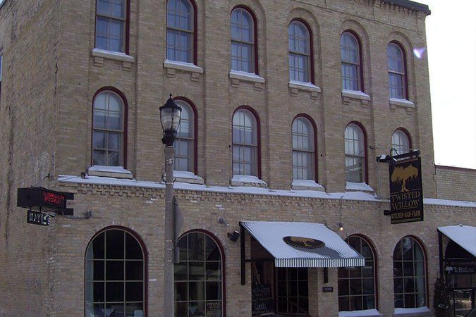 Brick building with arched windows, striped awning, and hanging sign on a snowy street corner