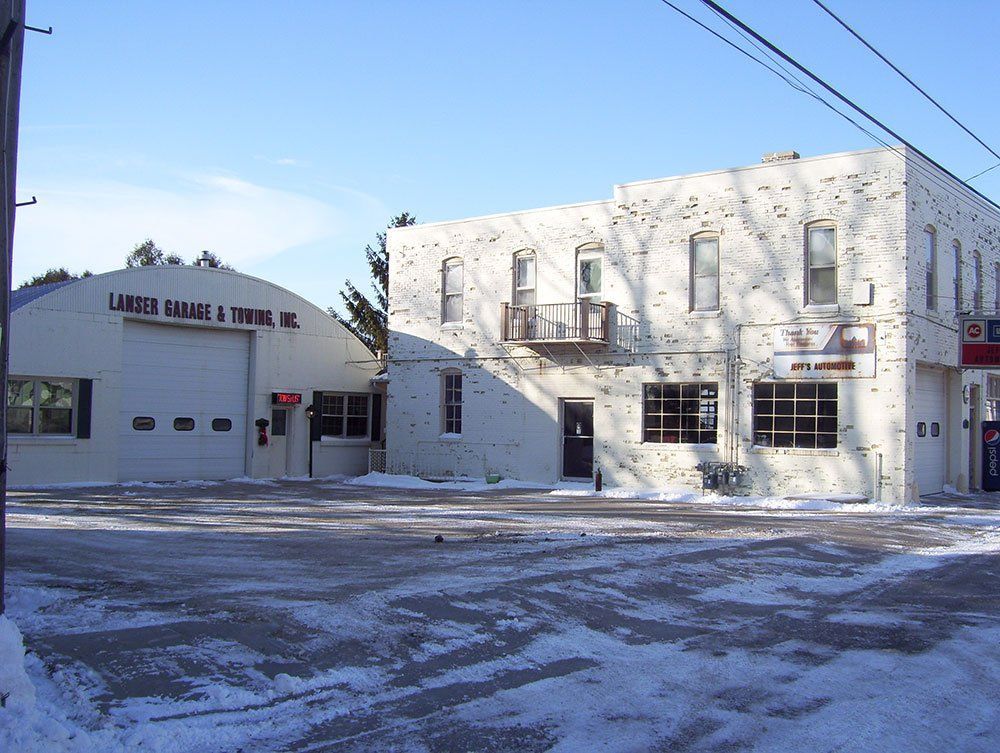 Snowy street view of a white building with garage bays and a sign reading “Lakes Marine & Tire Inc.”