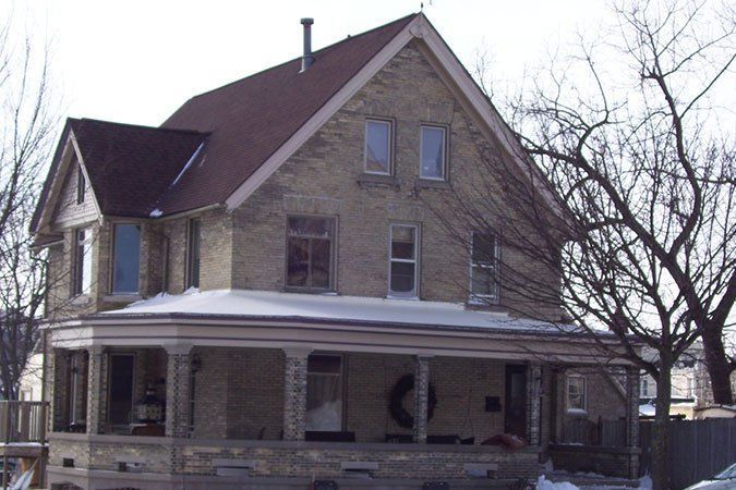 Stone house with a porch and snow on the roof in a winter yard