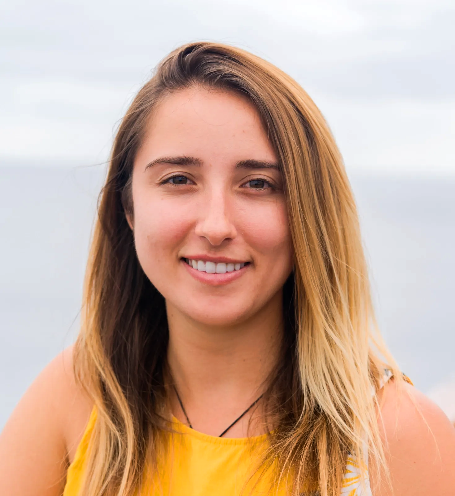 Smiling person in a yellow top against a cloudy sky background
