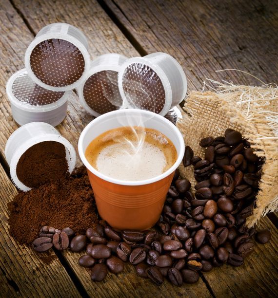 Tazza di caffè circondata da chicchi e baccelli su un tavolo di legno rustico, con fondi di caffè che si rovesciano nelle vicinanze.