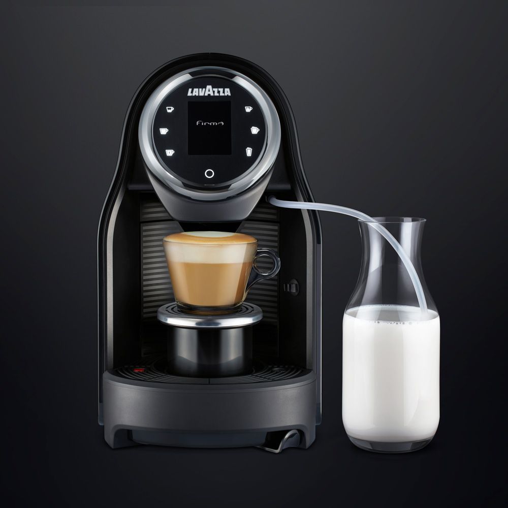 Macchina da caffè espresso compatta di colore nero, con un bicchiere di latte accanto, che prepara il caffè.