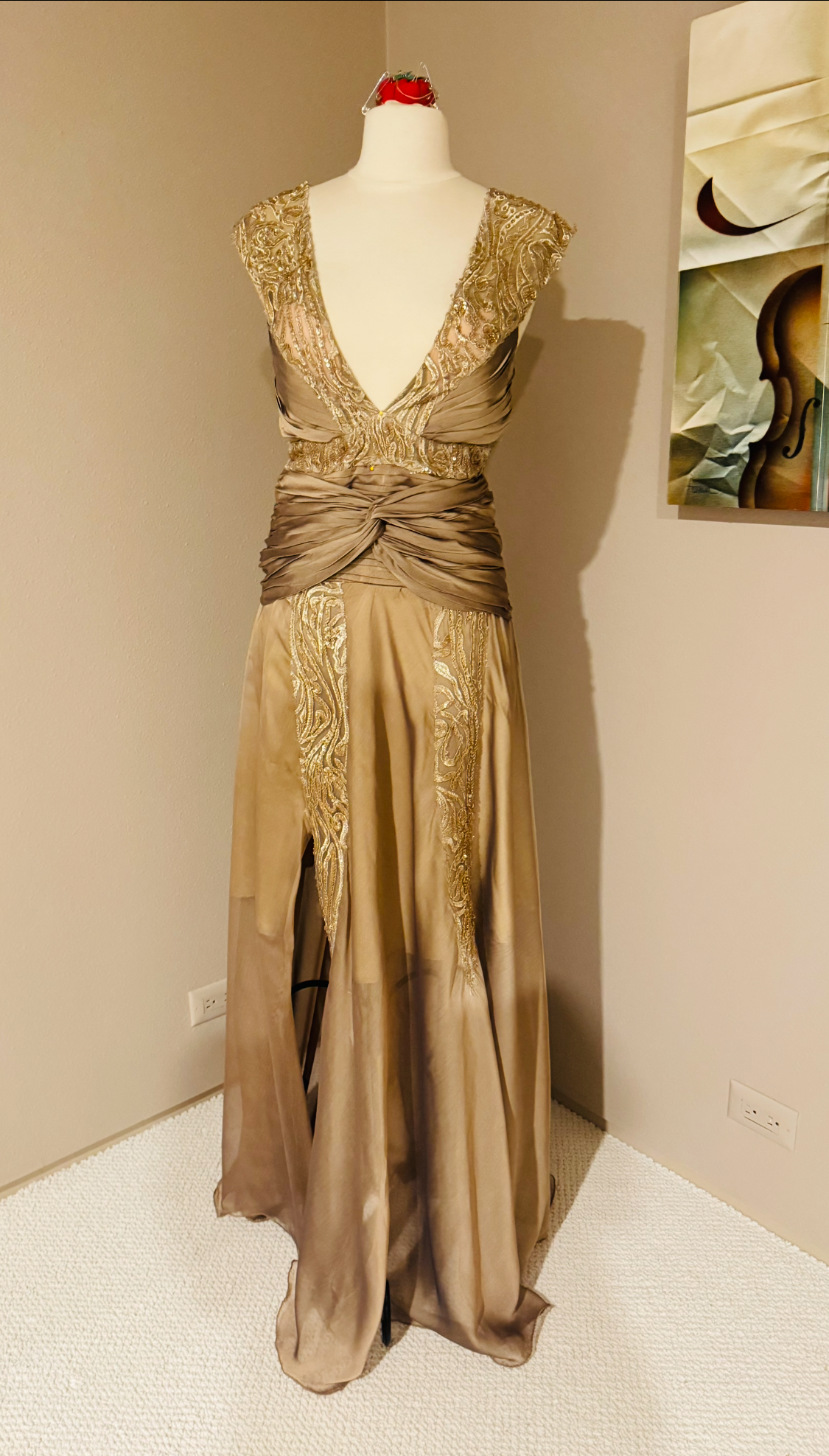 Gold sequined formal gown on a mannequin in a corner of a room, a painting on the wall behind.