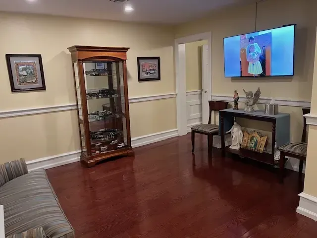 Living room with wood floors, display cabinet, gray sofa, and wall-mounted TV showing a colorful image