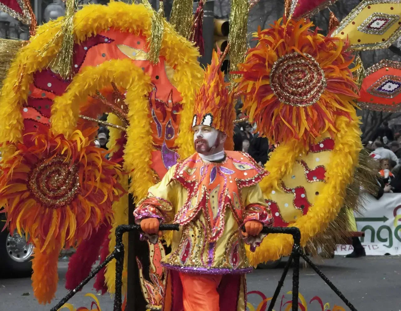 Person in bright orange costume with feathered wings and floral decorations in a parade